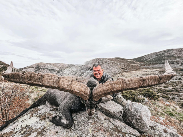Hunter posing with a large Spanish ibex trophy in rugged mountain terrain